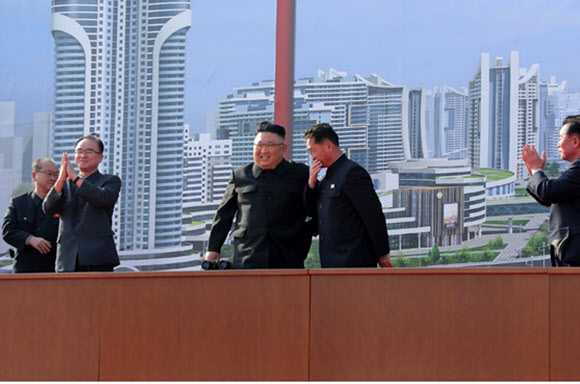 김정은 북한 국무위원장이 23일 수도 평양에 주택 1만세대를 짓는 착공식에 참석해 연설했다고 노동신문이 24일 보도했다. 김 위원장은 김덕훈 내각총리의 지근거리 보고를 들으며 흡족한 표정으로 서있다. 연단에는 발파 모습을 보는 데 사용한 듯한 쌍안경이 놓여있다. 2021.3.24   노동신문 홈페이지 캡처