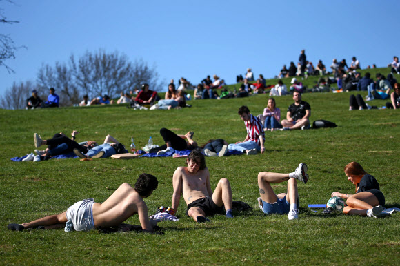 일광욕을 즐기는 사람들이 29일(현지시간) 런던의 프림로즈 힐에서 함께 앉아 따뜻한 날씨를 즐기고 있다. 영국의 세 번째 코로나19 봉쇄 제한이 완화됨에 따라, 최대 6명의 그룹이 밖에서 만날 수 있게 됐다. 영국은 빠른 예방접종으로 코로나19 봉쇄를 더욱 완화하기 시작했지만 나머지 유럽 정부는 코로나19 급증을 억제하기 위해 애를 쓰고 있다. AFP 연합뉴스