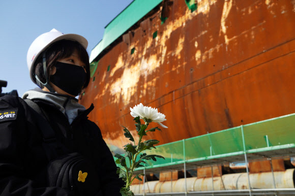 11일 오전 전남 목포시 목포신항에 인양된 세월호 선체 앞에서 4?16재단과 세월호 피해 가족들이 헌화와 묵념을 하며 피해자를 추모하고 있다. 피해 가족들은 이날 참사 해역에서 선상 추모식을 하려 했지만 해경이 사고 당시 현장지휘선으로 쓰인 ‘3009함’을 준비하자 탑승을 거부하고 세월호 선체 앞에서 추모식을 열었다. 2021.4.11  4·16 재단 제공