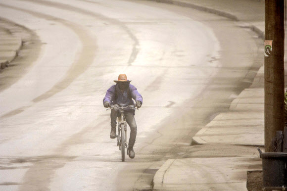 A man rides his bicycle on the main Black Rock road, covered with ash coming from the St. Vincent eruption of La Soufriere volcano, on the outskirts of Bridgetown, Barbados, Sunday, April 11, 2021. (AP Photo/Chris Brandis)/2021-04-12 08:23:40/ <연합뉴스
