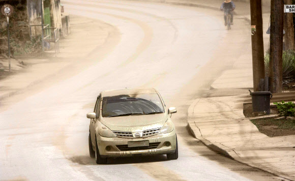 A vehicle drives on the main Black Rock road, covered with ash coming from the St. Vincent eruption of La Soufriere volcano, on the outskirts of Bridgetown, Barbados, Sunday, April 11, 2021. (AP Photo/Chris Brandis)