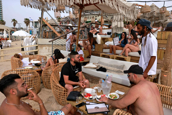 19일(현지시간) 이스라엘 텔아비브의 해변의 비치바에서 마스크를 쓰지 않은 시민들이 일광욕을 즐기고 있다. AFP 연합뉴스