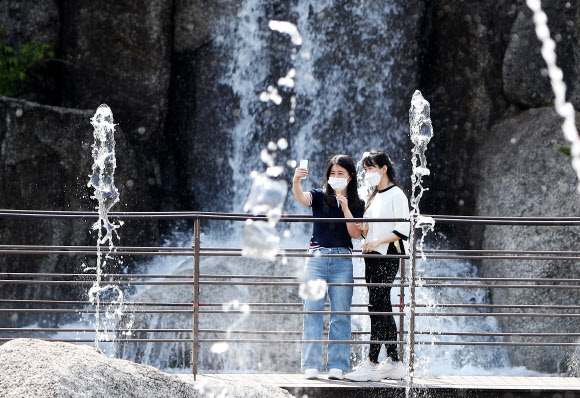 낮 기온이 20도 이상 오르며 초여름 같은 날씨를 보인 20일 오후 경기도 안산시 노적봉인공폭포공원에서 반팔 옷을 입은 시민들이 시원하게 쏟아지는 폭포수를 배경으로 사진을 찍고 있다. 2021.4.20  연합뉴스