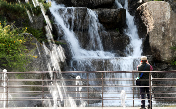 낮 기온이 20도 이상 오르며 초여름 같은 날씨를 보인 20일 오후 경기도 안산시 노적봉인공폭포공원을 찾은 시민들이 시원하게 쏟아지는 폭포수를 바라보고 있다. 2021.4.20  연합뉴스
