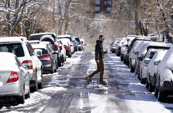 20일(현지시간) 미국 콜로라도주 덴버에 때아닌 눈보라가 몰아친 후 한 시민이 눈이 쌓인 거리를 가로질러 걷고 있다. AP 연합뉴스