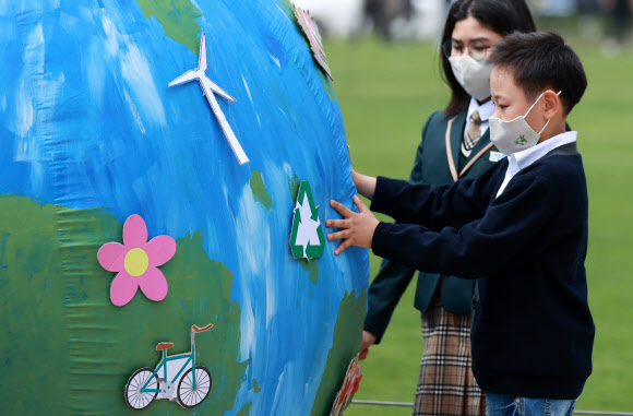 서울시와 녹색서울시민위원회 주최로 22일 오전 서울 중구 시청 앞 광장에서 열린 ‘2021 지구의 날 기념식’에서 참석자들이 지구 모형의 마스크를 벗기고 아픈 지구를 회복해 미래 세대인 청소년에게 전달하는 모습을 형상화해 상징의식을 펼치고 있다. 2021.4.22  연합뉴스