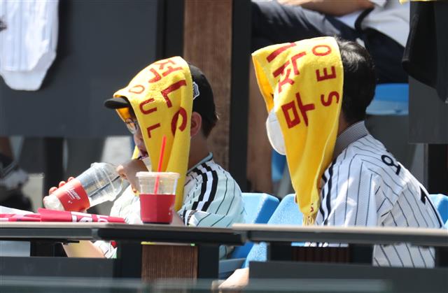 이른 더위가 찾아온 19일 서울 잠실야구장을 찾은 관람객들이 응원도구를 이용해 태양을 피하고 있다. 2021.5.19 뉴스1