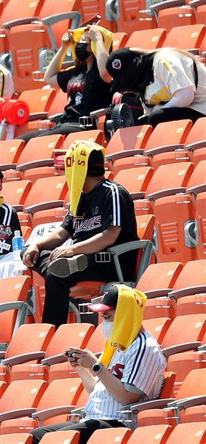 이른 더위가 찾아온 19일 서울 잠실야구장을 찾은 관람객들이 응원도구를 이용해 태양을 피하고 있다. 2021.5.19 뉴스1