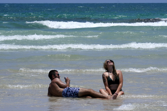한 커플이 26일(현지시간) 미국 플로리다 마이애미 해변의 모래사장에 앉아 해변을 즐기고 있다. AP 연합뉴스