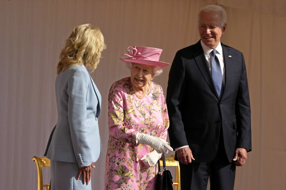 조 바이든(오른쪽) 미국 대통령이 13일(현지시간) 영국 런던 근교 윈저성에서 엘리자베스 2세 여왕과 환담하는 부인 질 바이든을 지켜보며 미소를 짓고 있다. 바이든 대통령은 이날 “여왕의 외모와 그 너그러움이 어머니를 떠올리게 한다”며 여왕을 백악관으로 초청했다고 밝혔다. 런던 AP 연합뉴스