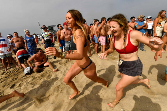 제47회 헤르모사비치 철인대회의 참가자들이 4일(현지시간) 미국 캘리포니아 헤르모사비치에서 공연을 보며 즐기고 있다. 40년 넘게 열린 이 비정규 3종 경기는 지난해 코로나19 대유행으로 취소된 뒤, 4일 재개됐다. 경쟁자들은 1마일을 달리고, 1마일을 서핑보드를 노를 젓고, 맥주 6팩을 마셔야 한다. 맥주를 토하는 사람들은 실격되지만, 누가 가장 잘 토하는가를 경쟁하는 사람들도 있다. AFP 연합뉴스