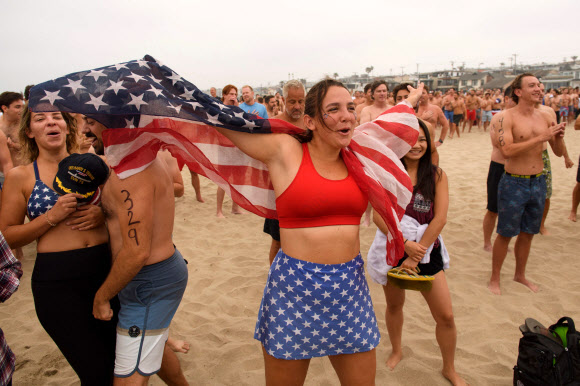 제47회 헤르모사비치 철인대회의 참가자들이 4일(현지시간) 미국 캘리포니아 헤르모사비치에서 경기 시작에 앞서 국가를 부르고 있다. 40년 넘게 열린 이 비정규 3종 경기는 지난해 코로나19 대유행으로 취소된 뒤, 4일 재개됐다. 경쟁자들은 1마일을 달리고, 1마일을 서핑보드를 노를 젓고, 맥주 6팩을 마셔야 한다. 맥주를 토하는 사람들은 실격되지만, 누가 가장 잘 토하는가를 경쟁하는 사람들도 있다. AFP 연합뉴스