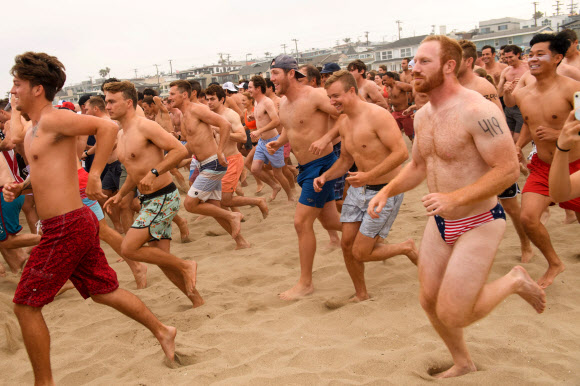 제47회 헤르모사비치 철인대회의 참가자들이 4일(현지시간) 미국 캘리포니아 헤르모사비치에서 달리고 있다. 40년 넘게 열린 이 비정규 3종 경기는 지난해 코로나19 대유행으로 취소된 뒤, 4일 재개됐다. 경쟁자들은 1마일을 달리고, 1마일을 서핑보드를 노를 젓고, 맥주 6팩을 마셔야 한다. 맥주를 토하는 사람들은 실격되지만, 누가 가장 잘 토하는가를 경쟁하는 사람들도 있다. AFP 연합뉴스