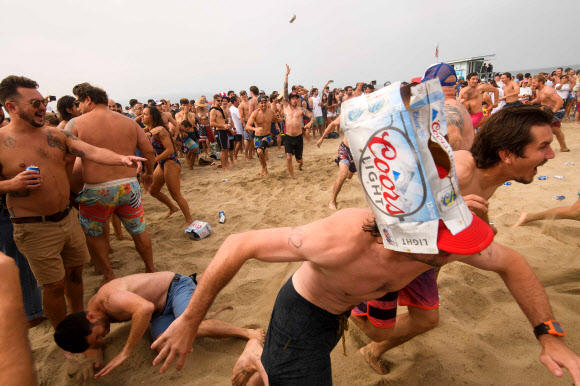 제47회 헤르모사비치 철인대회의 참가자들이 4일(현지시간) 미국 캘리포니아 헤르모사비치에서 공연을 보며 즐기고 있다. 40년 넘게 열린 이 비정규 3종 경기는 지난해 코로나19 대유행으로 취소된 뒤, 4일 재개됐다. 경쟁자들은 1마일을 달리고, 1마일을 서핑보드를 노를 젓고, 맥주 6팩을 마셔야 한다. 맥주를 토하는 사람들은 실격되지만, 누가 가장 잘 토하는가를 경쟁하는 사람들도 있다. AFP 연합뉴스