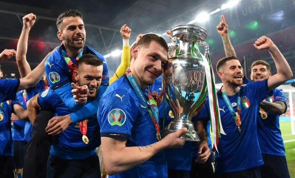 이탈리아 축구대표팀 안드레아 벨로티(토리노FC)가 12일(한국시간) 영국 런던 웸블리구장에서 열린 유로2020 결승에서 이탈리아가 잉글랜드를 승부차기 끝에 따돌리고 53년 만에 우승한 뒤 동료들이 환호하는 가운데 트로피를 들어 보이고 있다.  런던 EPA 연합뉴스