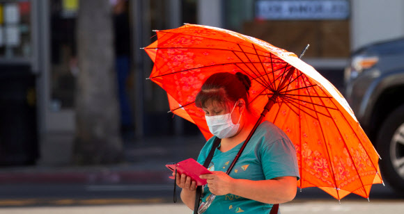 지난 3월 31일(현지시간) 미국 캘리포니아주 로스앤젤레스의 한 여성이 마스크를 쓴 채 양산을 받쳐 들고 휴대전화를 만지작거리고 있다. 로이터 자료사진 연합뉴스 