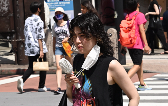 도쿄 시부야역 인근을 걷는 한 시민이 마스크를 내리고 손선풍기로 더위를 식히고 있다.