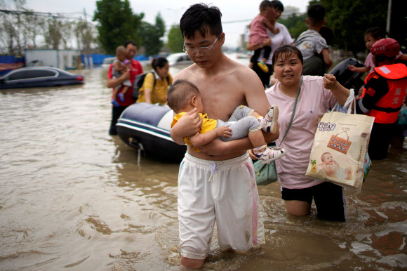 22일 중국 중부 허난성 정저우에서 수해 피해를 입은 한 남성이 아이를 안고 안전한 장소로 대피하고 있다. 정저우 로이터 연합뉴스