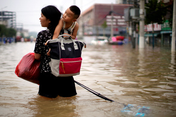 지난 23일 중국 허난성 정저우에서 한 여성이 폭우로 물에 담긴 도로를 아이를 안고 건너고 있다. 정저우 로이터 연합뉴스