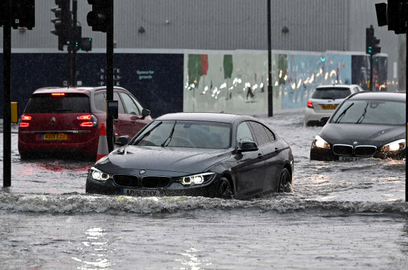 25일(현지시간) 영국 런던 나인 엘름스 지역에서 차량들이 폭우로 물에 잠긴 도로를 헤쳐나가고 있다. AFP 연합뉴스
