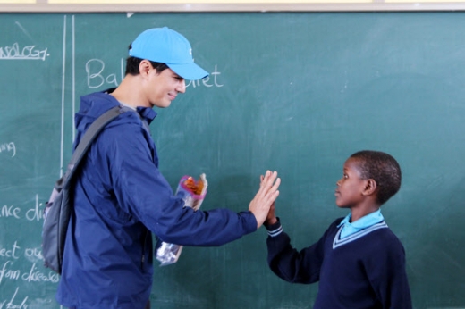 배우 조인성(왼쪽)이 2019년 탄자니아의 싱기다 뉴비전스쿨을 방문해 학생과 손을 마주치고 있다.<br>밀알복지재단 제공