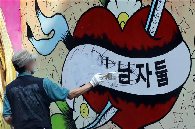 30일 오전 서울 종로구의 한 서점 벽면에 그려진 윤석열 전 검찰총장의 배우자 김건희 씨를 비방하는 내용의 벽화 문구를 서점 관계자가 페인트로 지우고 있다. 2021.7.30 뉴스1