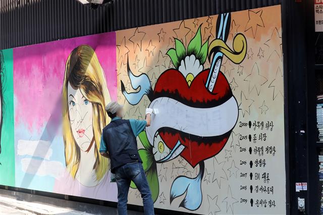 30일 오전 서울 종로구의 한 서점 벽면에 그려진 윤석열 전 검찰총장의 배우자 김건희 씨를 비방하는 내용의 벽화 문구를 서점 관계자가 페인트로 지우고 있다.  2021.7.30 뉴스1