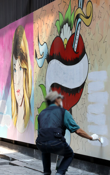 서울 종로구의 한 서점 외벽에 그려진 대권 주자 윤석열 예비후보의 부인 김건희 씨를 비방하는 내용의 벽화가 논란이 되고 있는 가운데 30일 오전 한 건물 관계자가 벽화의 글자를 흰색 페인트로 칠하고 있다. 2021.7.30  연합뉴스