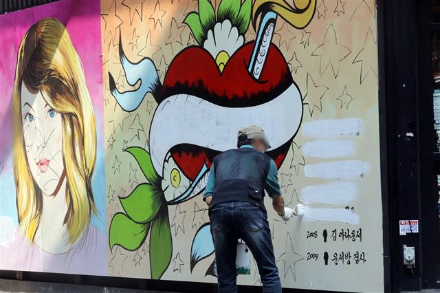 30일 오전 서울 종로구의 한 서점 벽면에 그려진 윤석열 전 검찰총장의 배우자 김건희 씨를 비방하는 내용의 벽화 문구를 서점 관계자가 페인트로 지우고 있다.  2021.7.30 뉴스1