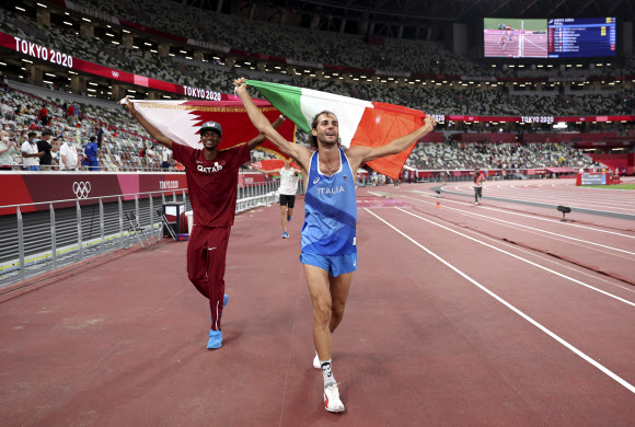지난 1일 일본 도쿄 올림픽 스타디움에서 열린 올림픽 육상 남자 높이뛰기 결선에서 2m37의 기록으로 109년만에 육상 종목 공동 금메달을 딴 이탈리아의 지안마르코 탬베리(오른쪽)와 카타르의 무타즈 바르심(왼쪽)이 각자의 국기를 높이 들고 경기장을 돌고 있다. 도쿄 AP 연합뉴스