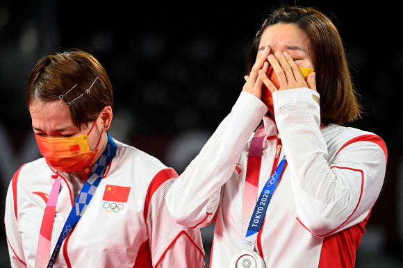 경기 도중 기합을 가장해 욕설을 내뱉어 논란을 자초한 중국 배드민턴 선수 천칭천(왼쪽)이 2일 2020 도쿄올림픽 여자복식 결승전에서 그레이시아 폴리-아프리야니 라하유(인도네시아) 조에 0-2로 완패한 뒤 은메달을 목에 건 채 고개를 숙이며 침통해 하고 있다. 그와 조를 이룬 판자이는 눈물이 쏟아지는 듯 눈을 가리고 있다. 도쿄 AFP 연합뉴스 