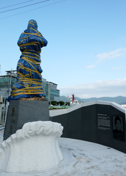 경남 창원시 마산합포구 중앙부두에 3·15 부정선거를 규탄하는 시위에 참여했다 얼굴에 최루탄이 박혀 숨진 채 마산만에 떠오른 김주열 열사 동상이 동상 추모판 문구를 둘러싸고 지역 민주운동 단체가 대립하면서 완성되고도 비닐과 테이프로 꽁꽁 감겨 한 달째 서 있다. 사진은 11일 오후 촬영. 2021.8.12  연합뉴스