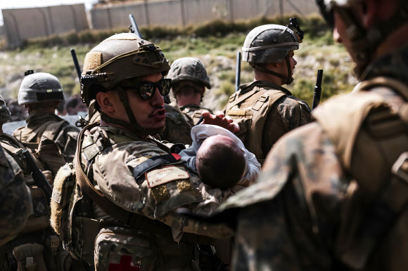20일(현지시간) 아프가니스탄 수도 카불의 하미드 카르자이 국제공항을 경비하는 미국 해병대원이 아기를 품에 안고 달래고 있다.  AP 연합뉴스