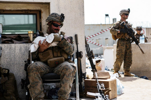 20일(현지시간) 아프가니스탄 수도 카불의 하미드 카르자이 국제공항을 경비하는 미국 해병대원이 아기를 품에 안고 달래고 있다.  AFP 연합뉴스