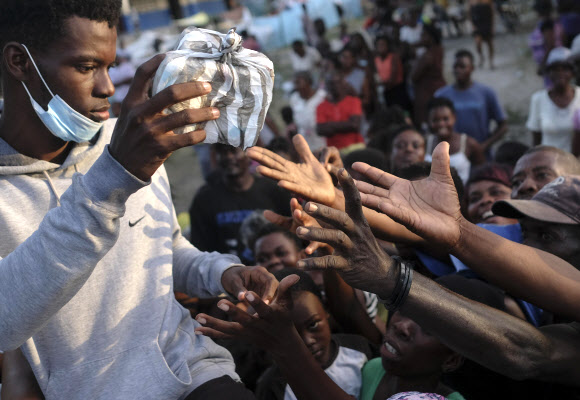 지진으로 고통받고 있는 아이티의 남부 해안도시 레카이에서 21일(현지시간) 구호용 식료품 꾸러미를 받으려고 필사적으로 손을 내밀고 있는 이재민들. 레카이 AP 연합뉴스