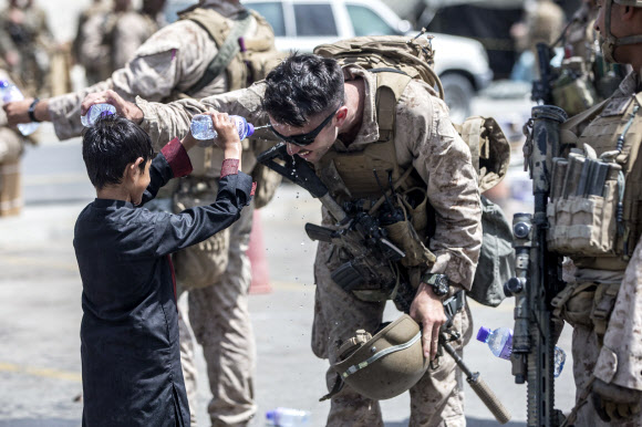 아프가니스탄 카불 공항의 혼잡한 상황을 진정시키기 위해 투입된 미군 해병대 병사가 지난 21일(현지시간) 현지인 소년과 서로의 머리에 생수를 뿌려 더위를 식혀주고 있다. 미군 해병대 제공 AP 연합뉴스 