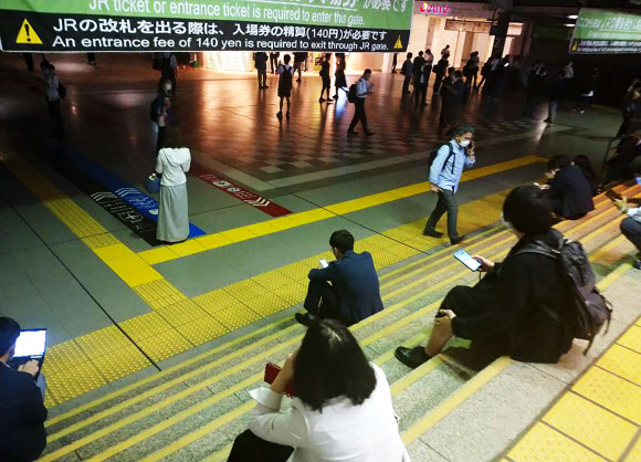 일본 도쿄에서 열차 승객들이 7일 지진으로 인해 지연된 열차 운행을 계단에 앉아 기다리고 있다. 강진은 7일 밤 도쿄도를 강하게 흔들었지만 쓰나미가 발생하지는 않았다. AP 연합뉴스 2021-10-07