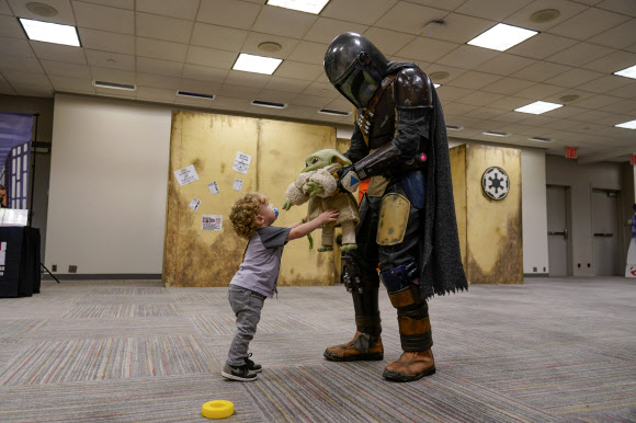 Miles Fourquet, 1, plays with a doll held by a man dressed as the Mandalorian at New York Comic Con in New York, Friday, Oct. 8, 2021. Although the convention was cancelled last year because of COVID-19, this year attendees were welcomed back with mandatory masking and proof of vaccination. (AP Photo/Seth Wenig)