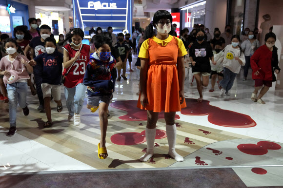태국 방콕의 한 백화점에서 할로윈 행사가 열린 가운데 넷플릭스 한국 드라마 ‘오징어 게임’의 술래 복장을 한 소녀가 손님들과 ‘무궁화 꽃이 피었습니다’ 게임을 하고 있다. AP 연합뉴스