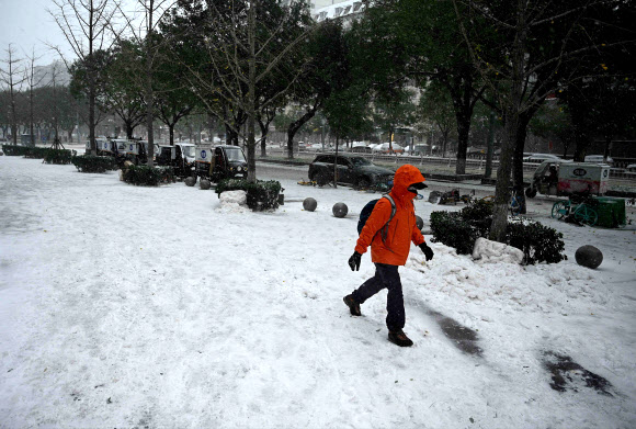 한 시민이 7일(현지시간) 때이른 눈이 내린 중국 베이징 거리를 걷고 있다. AP 연합뉴스