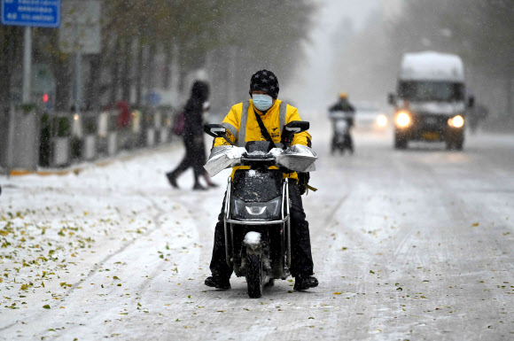 시민들이 7일(현지시간) 때이른 눈이 내린 중국 베이징 거리를 걷고 있다. AFP 연합뉴스