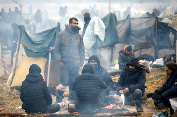18일(현지시간) 벨라루스 그로드노 지역의 폴란드 국경 인근에 마련된 난민 캠프에서 중동 출신 이민자들이 모닥불 주위에 모여 앉아 있다. 그로드노 로이터 연합뉴스