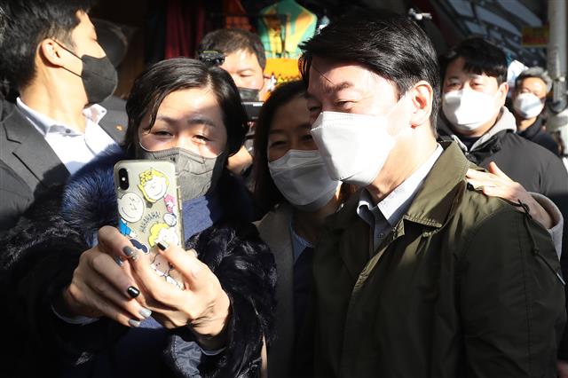 안철수 국민의당 대선 후보가 부인 김미경 교수가 20일 오후 대구 중구 서문시장을 찾아 시민들과 인사를 나누던 중 한 시민의 기념사진 요청에 안철수 대표의 얼굴이 휴대전화 카메라 앵글에 들어오지 않자 김미경 교수가 안 대표 목덜미를 잡아당긴 뒤 어깨 위에 손을 올려 포즈를 취하고 있다. 2021.12.20 뉴스1