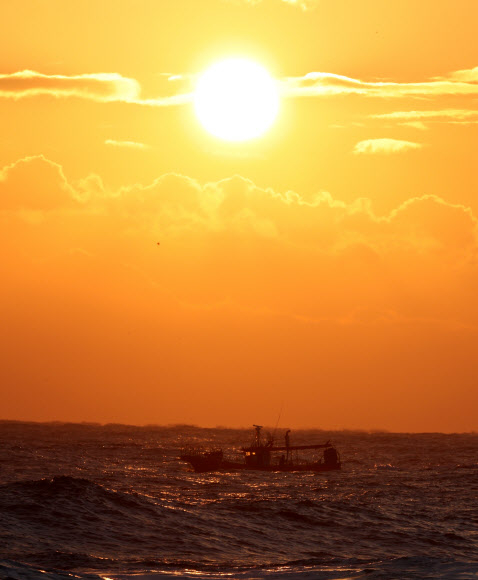 22일 강원 강릉시 사천해변 앞바다에서 높은 파도와 짙은 구름을 뚫고 붉은 해가 솟아오르는 가운데 어선이 조업을 나가고 있다. 2021.12.22 연합뉴스