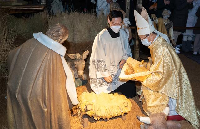 정순택 서울대교구장 대주교가 25일 서울 명동성당 앞마당에서 아기 예수를 말구유에 안치하는 구유 예절의식을 하고 있다. 2021.12.25  뉴스1