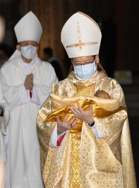 정순택 서울대교구장 대주교가 25일 서울 명동성당 앞마당에서 아기 예수를 말구유에 안치하는 구유 예절의식을 하고 있다. 2021.12.25 뉴스1
