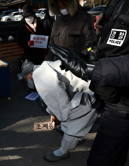13일 오후 서울 종로구 견지동 조계사 앞에서 ‘승려대회 취소를 요구하는 불제자’라는 이름으로 모인 승려와 불교 신도들이 “코로나 시국에 국민을 불안하게 하는 승려대회를 취소하라”고 요구하며 기자회견을 하던 중 회견 내용에 반대하는 한 승려가 다가와 회견 참석자가 들고 있던 팻말을 뺏어 찢은 뒤 회견 중단을 요구했다. 회견 참가자와 실랑이 뒤 팻말을 찢은 승려가 ‘조계종’이란 문구가 적힌 팻말 조각을 줍고 있다. 2022.1.13  연합뉴스