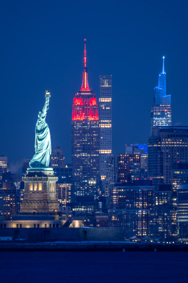 31일(현지시간) 미국 뉴욕의 자유의 여신상 너머로 첨탑을 붉게 밝힌 엠파이어스테이트 빌딩이 보인다. 뉴욕 신화 연합뉴스