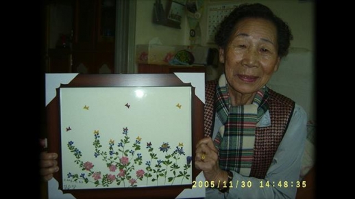 다큐멘터리 영화 ‘보드랍게’의 주인공 김순악 할머니가 생전 즐겨 작업하던 압화 작품을 들고 있는 모습. 인디플러그 제공