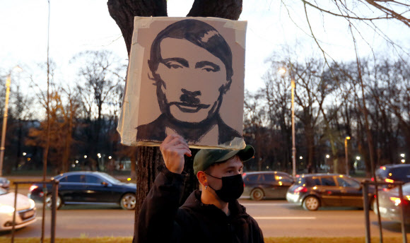 루마니아의 한 인권운동가가 24일(현지시간) 수도 부쿠레슈티의 우크라이나대사관 앞에서 블라디미르 푸틴 러시아 대통령과 나치 독일의 독재자 히틀러를 섞은 그림을 들고 있다. 부쿠레슈티 EPA 연합뉴스